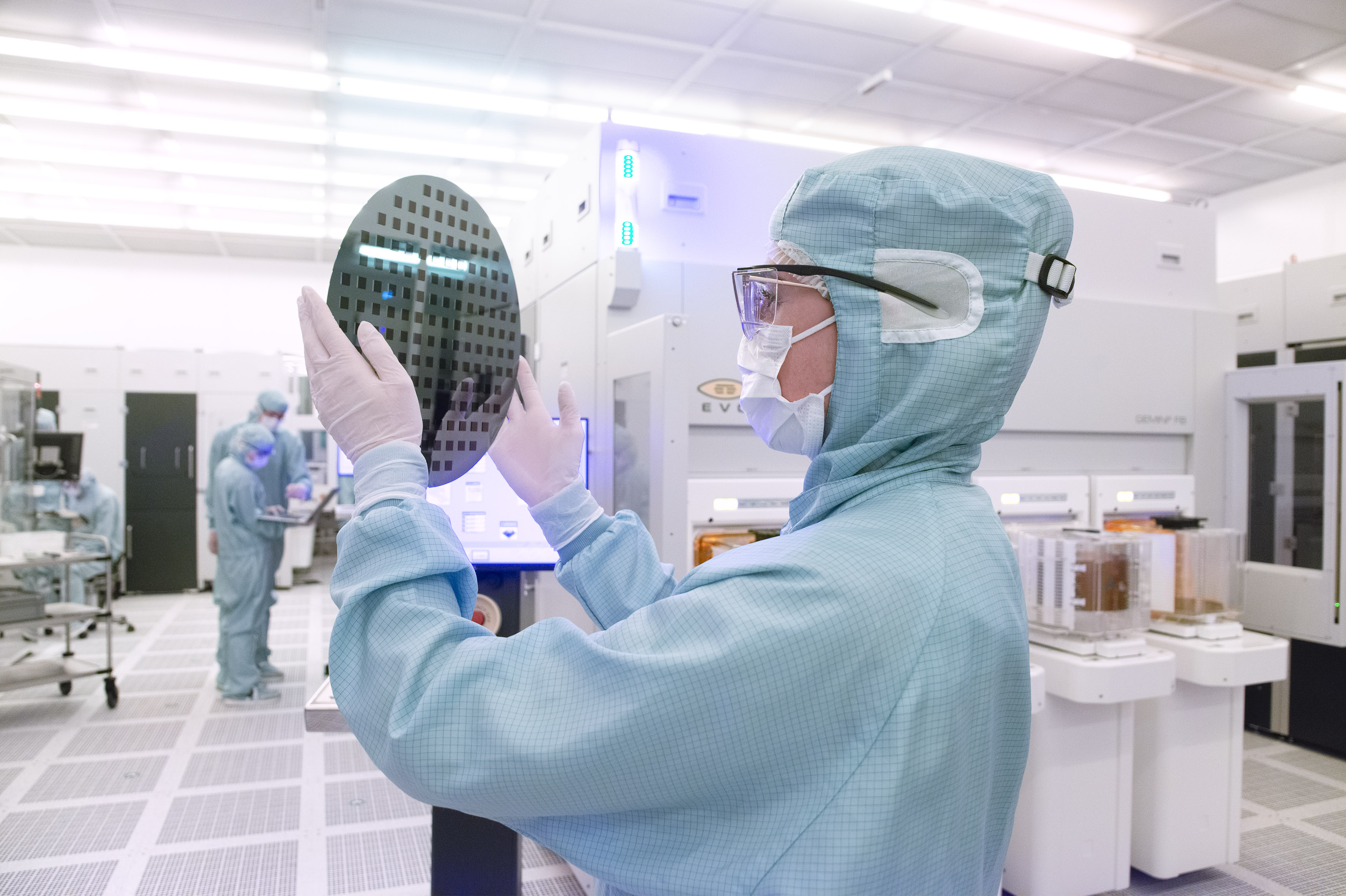 Mitarbeiterin in Reinraumkleidung prüft Siliziumwafer in einem Labor in Österreich